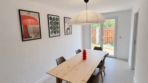 A dining area with a long wooden table, six chairs, a hanging light fixture, and framed artwork on the walls.