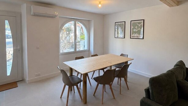 A spacious room with a wooden ceiling, a dining table with chairs, a sofa, and a window with a view.