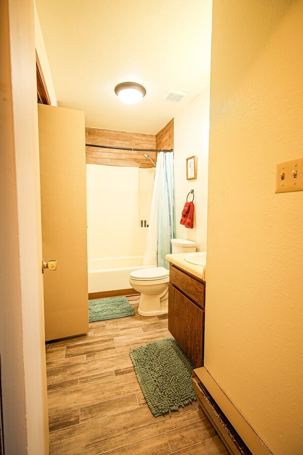 A bathroom with a wooden floor, a bathtub, a toilet, and a sink.