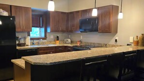Una cocina moderna con armarios de madera, un refrigerador negro, un microondas, un tostador y una encimera de granito.
