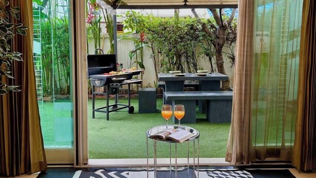 Une pièce avec vue sur un jardin, un barbecue et une table avec des boissons.