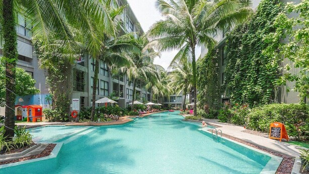 A swimming pool surrounded by palm trees and a building with a covered area. - Comfy 1BR Getaway by Beach & Shops- diamond C176 (Tambon Choeng Thale)