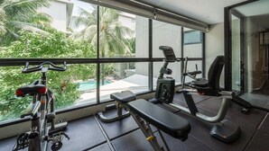 A gym with exercise equipment, a bench, and large windows overlooking a pool and greenery. - Comfy 1BR Getaway by Beach & Shops- diamond C176 (Tambon Choeng Thale)