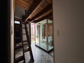 A hallway with a wooden ceiling, a ladder, a patterned floor, and a glass-enclosed shower area. - Elegant San Juan Loft for 8 • The Mezzanine (San Juan de Puerto Rico)