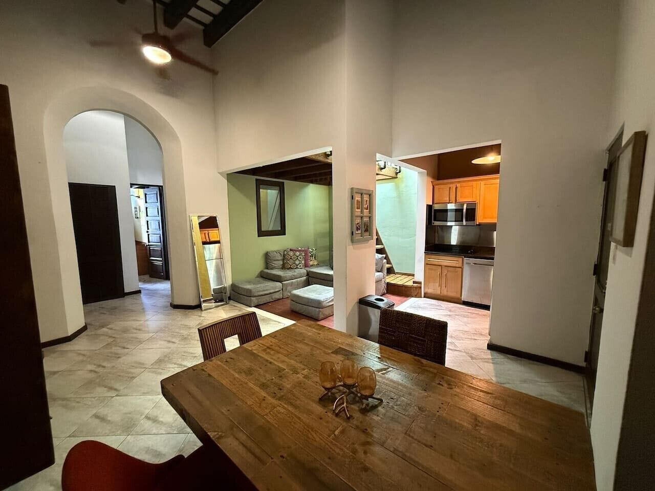 A spacious living area with a wooden dining table, a sofa, and a kitchen in the background.