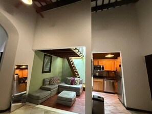 A compact living space with a sofa, ottoman, and a staircase leading to a kitchen area. - Elegant San Juan Loft for 8 • The Mezzanine (San Juan de Puerto Rico)