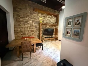 A room with a stone wall, a wooden dining table, chairs, a television, and framed pictures on the wall. - Elegant San Juan Loft for 8 • The Mezzanine (San Juan de Puerto Rico)
