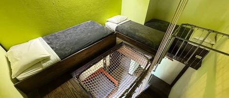 Una cambra petita i tancada amb un llit superposat, una barana de seguretat metàl·lica i una zona amb mosquitera.