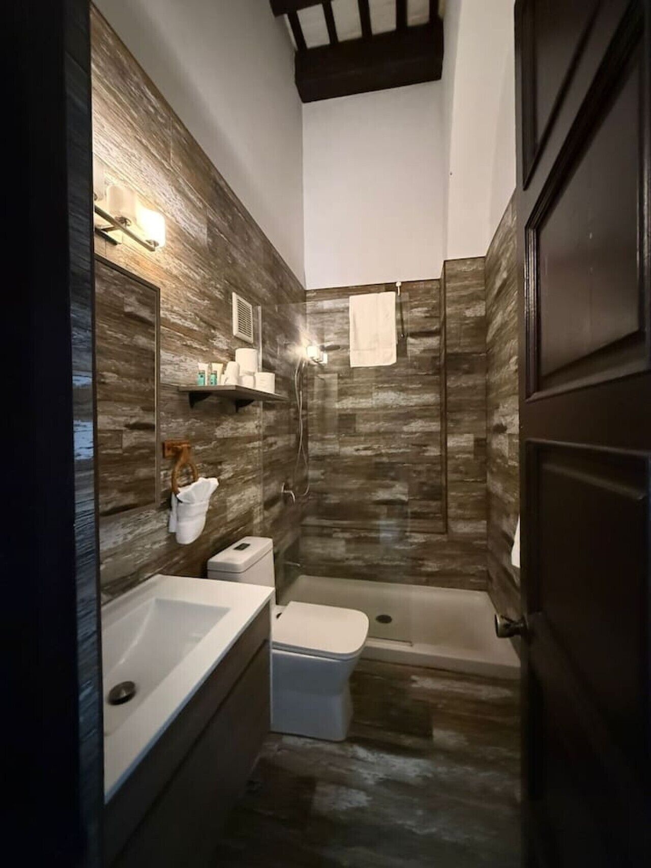 A bathroom with a shower, toilet, and sink, featuring a wooden wall design and a towel hanging on the wall.