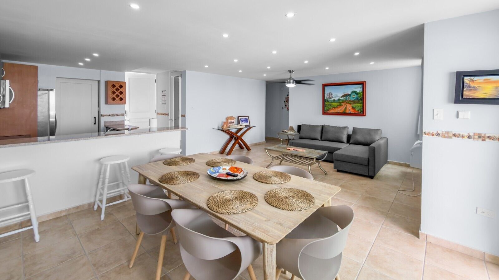 A modern kitchen with a dining area, grey furniture, and a grey sofa in the living room.