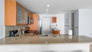 A modern kitchen with granite countertops, stainless steel appliances, wooden cabinets, and a built-in oven. - Hillside Village Hideaway | Sleeps 8 Comfortably (Mameyes II)