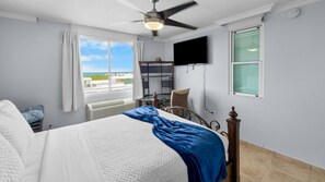 A bedroom with a bed, a ceiling fan, a TV, a window with curtains, and a view of the outside. - Hillside Village Hideaway | Sleeps 8 Comfortably (Mameyes II)