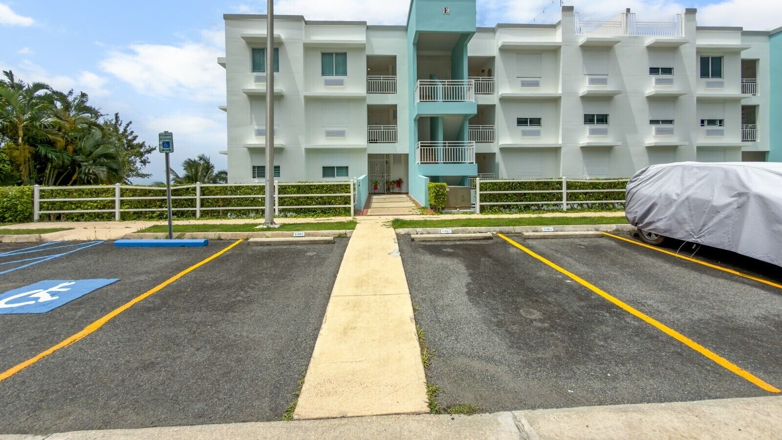 Un parking avec des places réservées aux personnes handicapées, un abri pour voitures et un immeuble doté de plusieurs balcons.