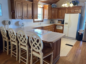A kitchen with wooden cabinets, a central island with chairs, a microwave, a refrigerator, and a sink.