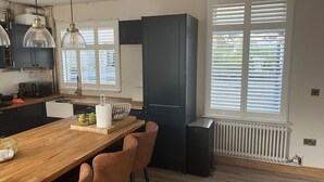 Eine moderne Küche mit einem Holztisch, Barhocker, einem schwarzen Kühlschrank und einem Fenster mit Jalousien.