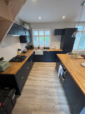 Una cocina moderna con armarios oscuros, encimera de madera, estufa a gas y una ventana con persianas.