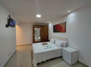 A hotel room with a bed, a small bedside table, a wall-mounted TV, a painting, and a door leading to another room. - Suíte com Jacuzzi Vista de Escarpas 4 (Capitólio)