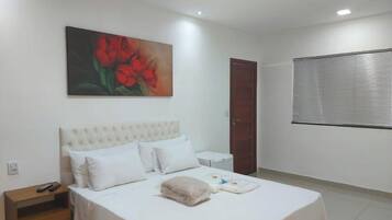 Un dormitorio con cama, mesita de noche, un cuadro, una puerta y una ventana con persianas.