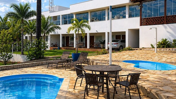 A modern building with a swimming pool, outdoor seating, and palm trees.