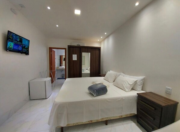 A bedroom with a bed, a dresser, a TV, and a small refrigerator. - Suíte com Jacuzzi Vista de Escarpas 3 (Capitolio)