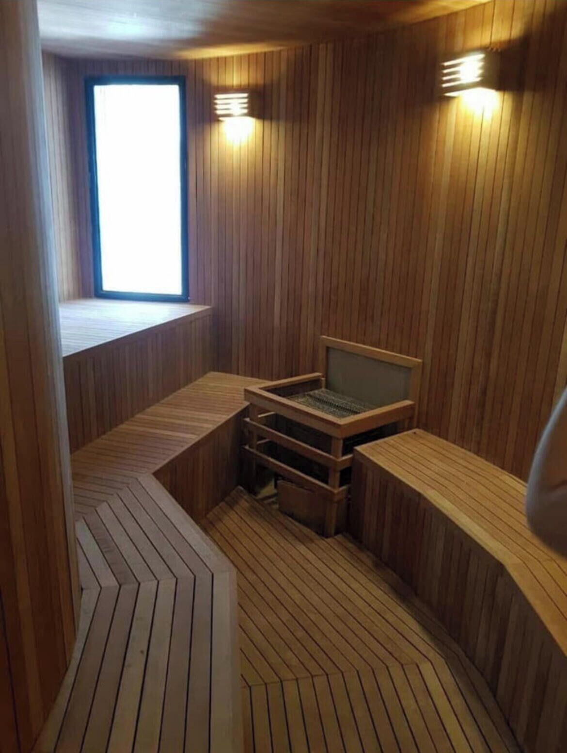 A sauna room with wooden walls, a bench, and a window.