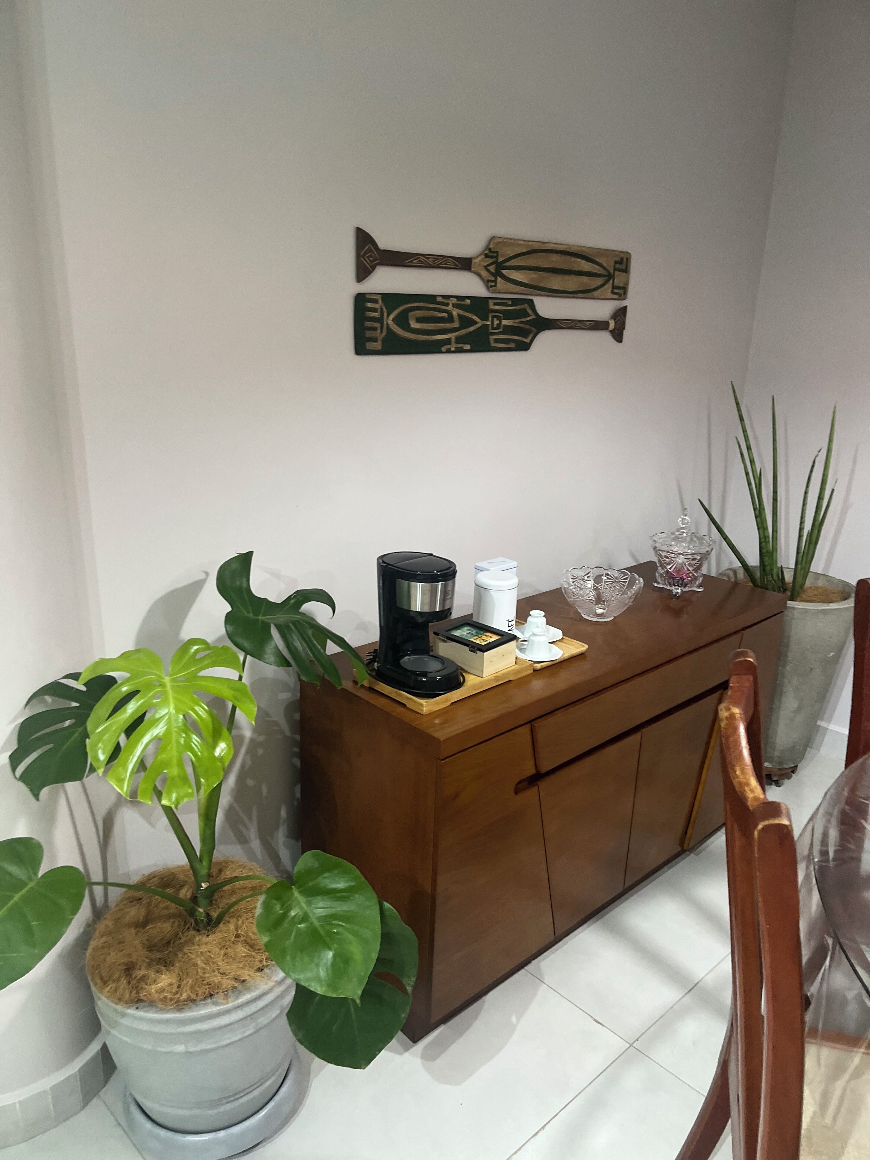 Un coin de pièce avec un meuble en bois, une machine à café, une plante en pot et un élément décoratif fixé au mur.