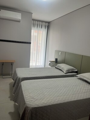 Ein Hotelzimmer mit zwei Betten, einem Schreibtisch, einer Klimaanlage und einem Fenster mit Vorhängen.