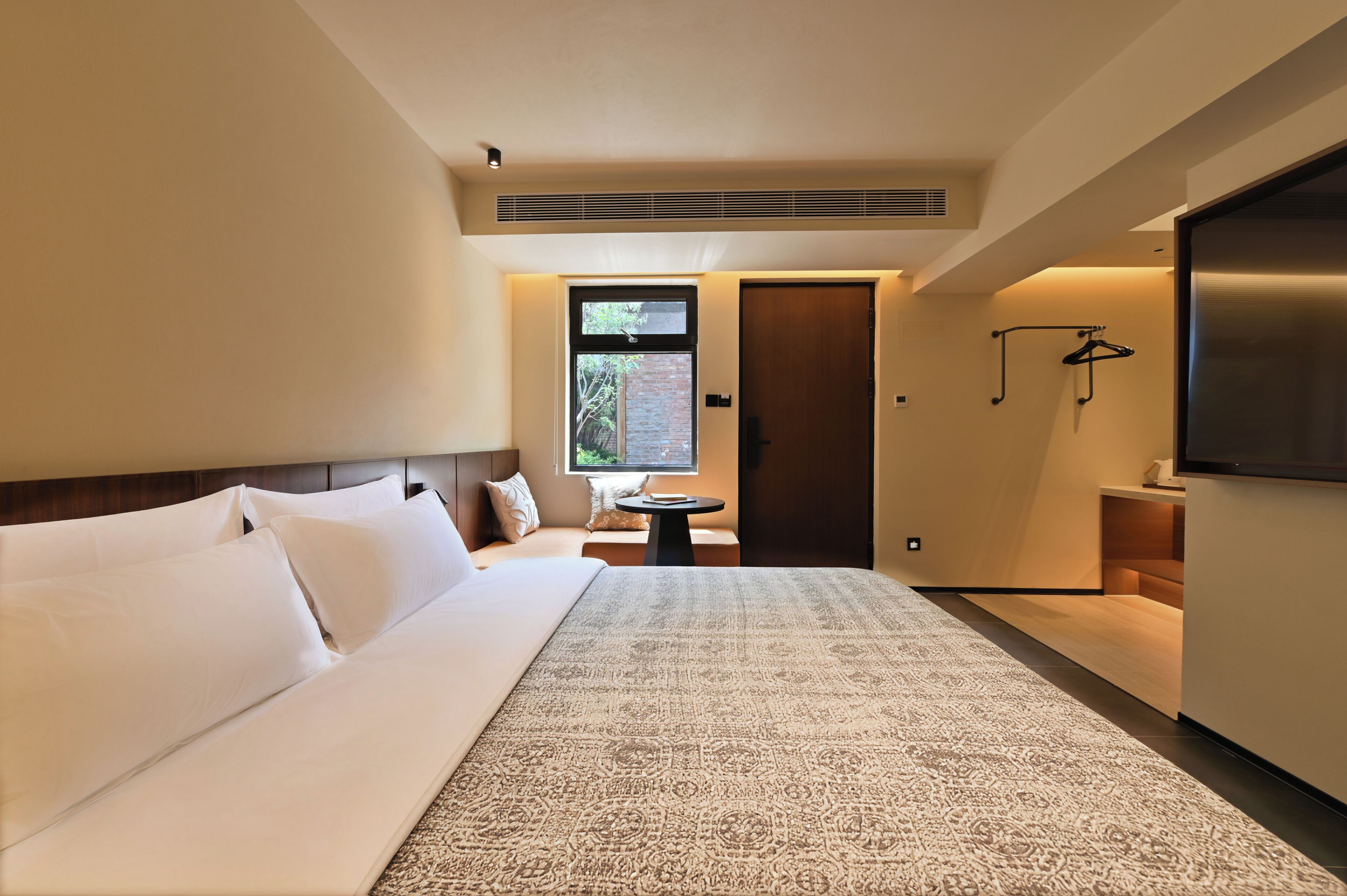 A modern hotel room with a large bed, a small round table, a TV, and a window with a view.