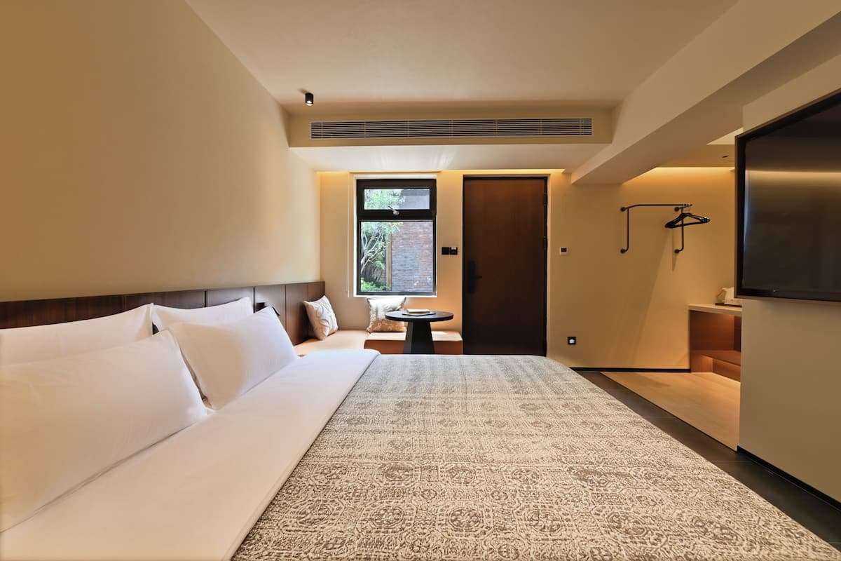 Una habitación de hotel moderna con una cama grande, una mesa redonda pequeña, un televisor y una ventana con vistas.