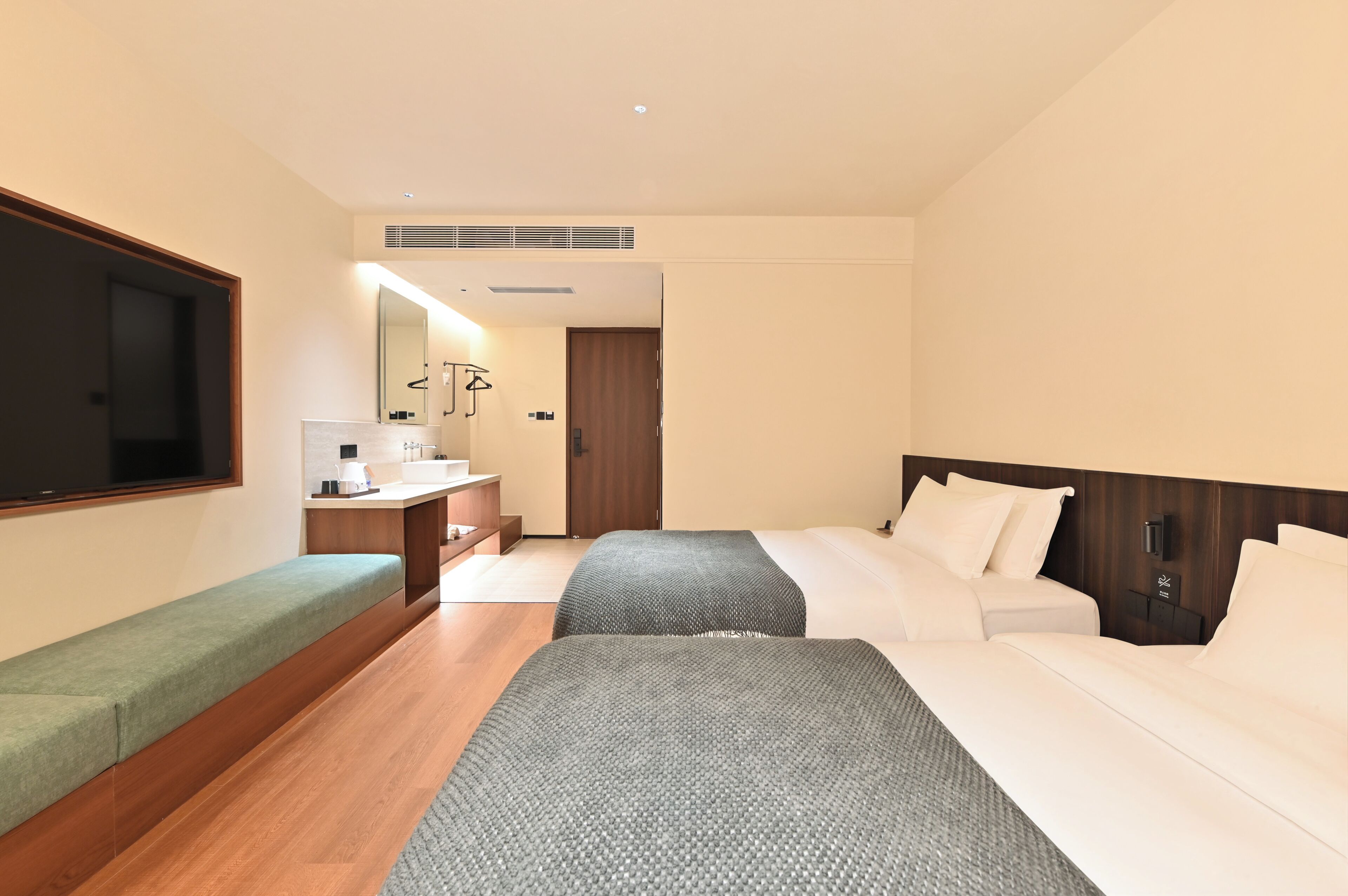 A hotel room with a bed, a bench, a desk with a mirror, and a television.
