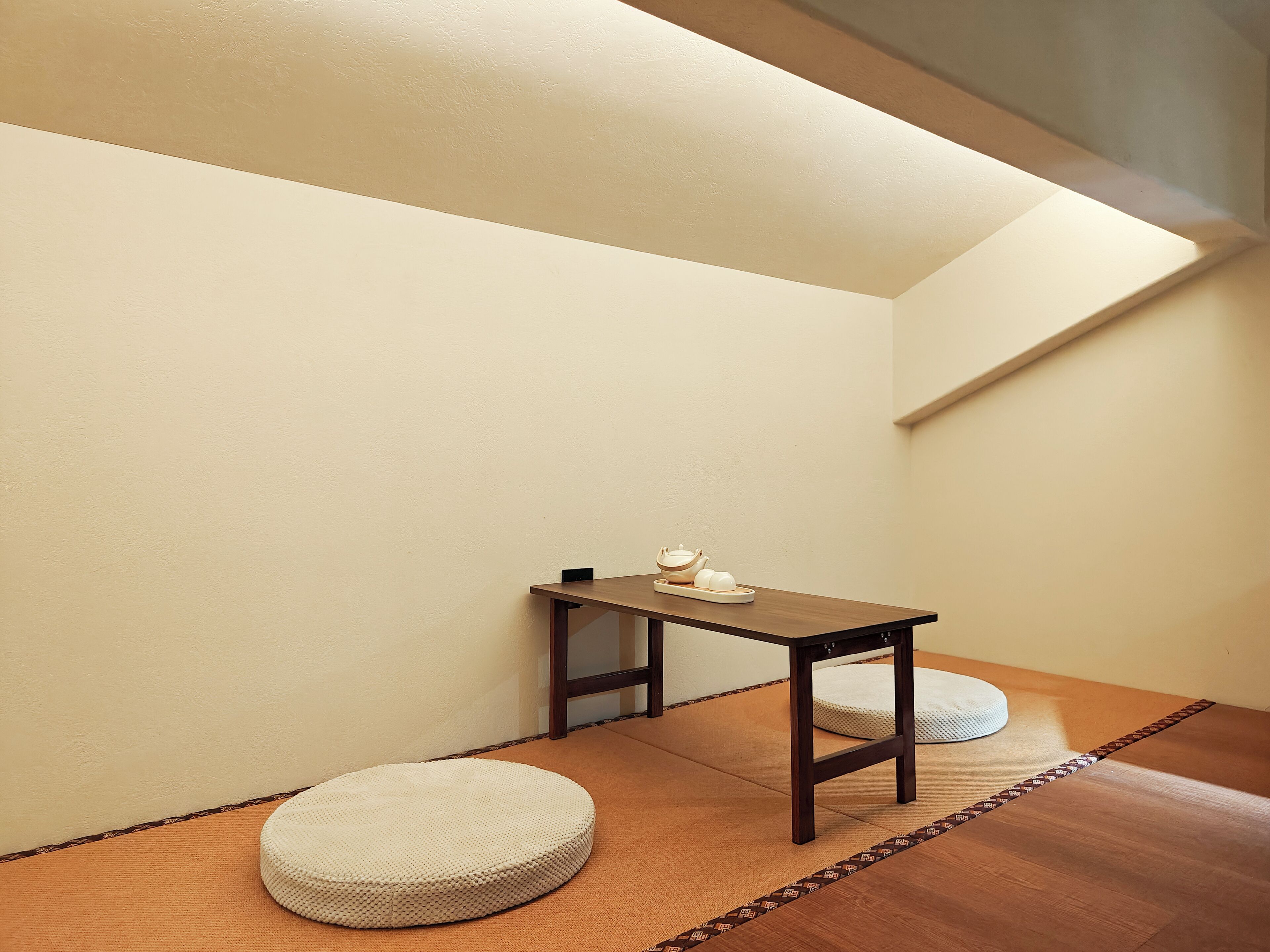 Una habitación pequeña con una mesa de madera, dos cojines redondos y suelo de esteras de tatami.