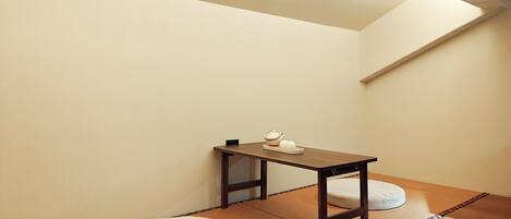 Una habitación pequeña con una mesa de madera, dos cojines redondos y suelo de esteras de tatami.