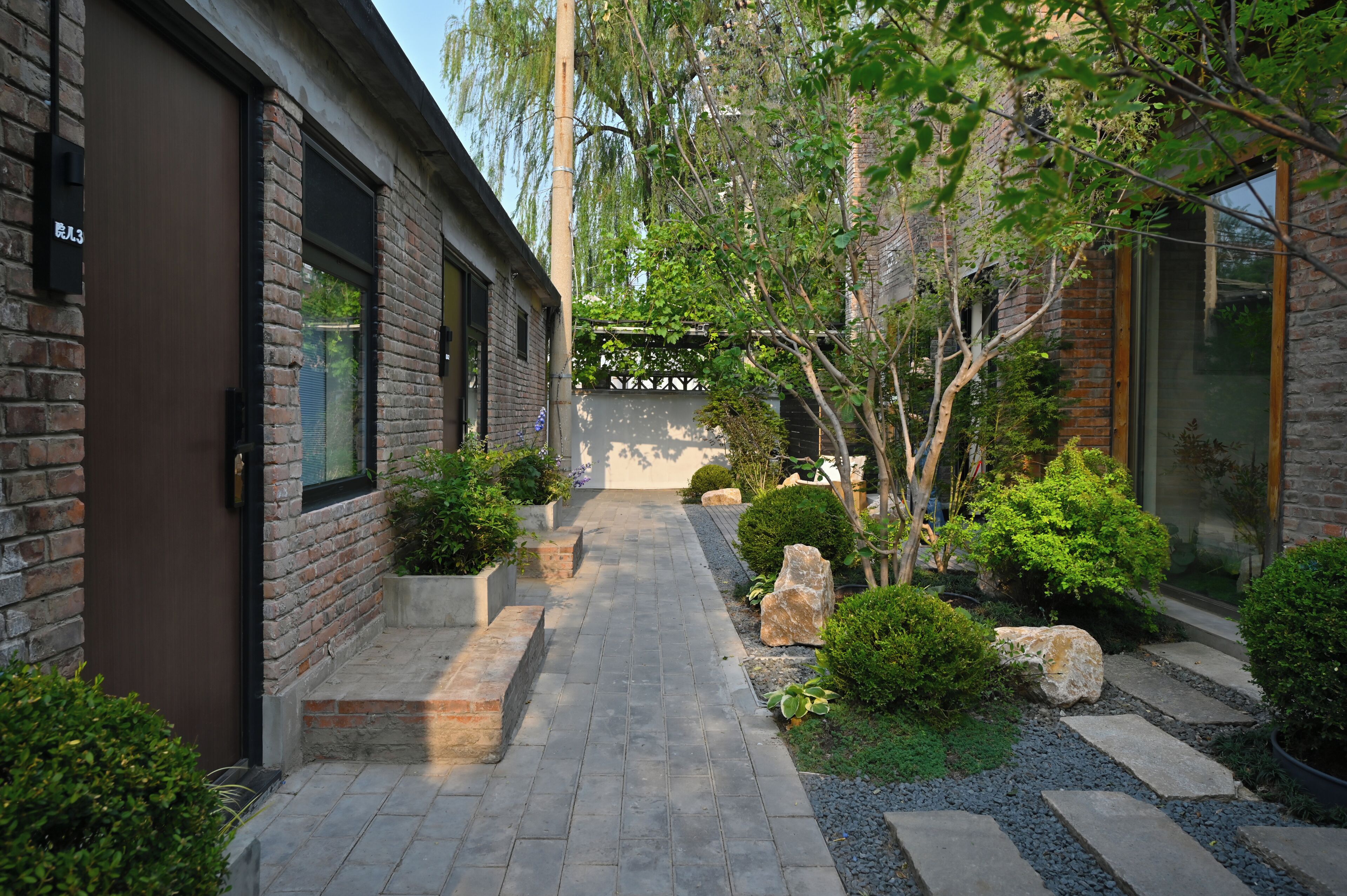 A narrow pathway leading to a building with brick walls and large windows.