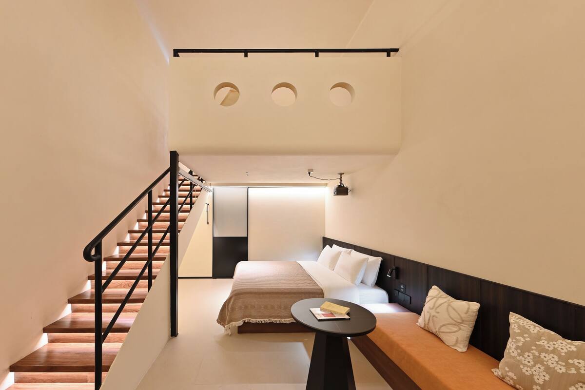 Una habitación de hotel moderna con una escalera de madera, una cama con cabecero, una mesita pequeña y un sofá.
