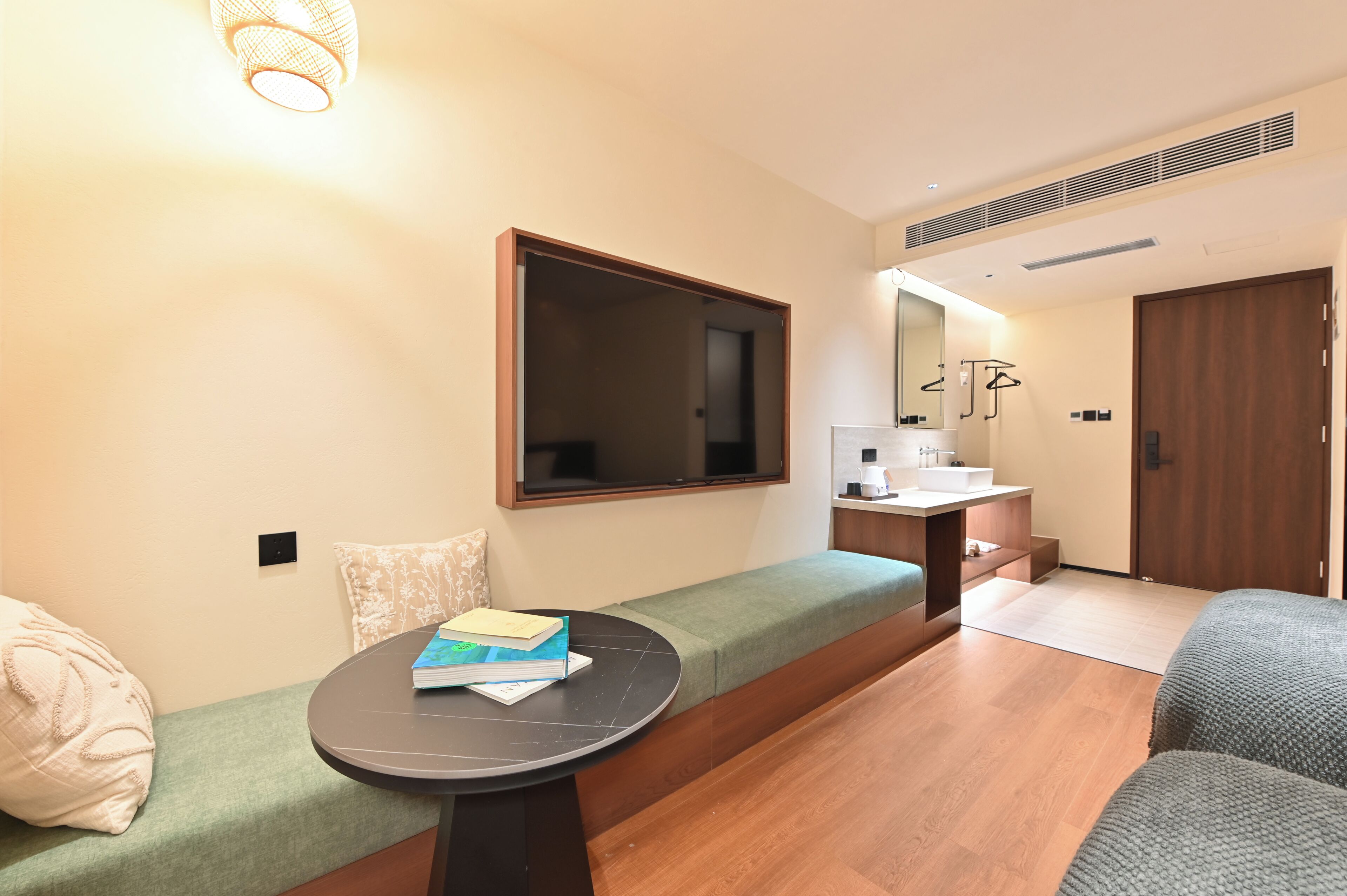 A modern room with a sofa, a small table, a TV, a kitchenette, and a large mirror.