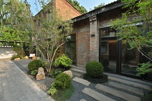 A modern building with a brick exterior, large windows, and a well-maintained garden with rocks and shrubs. - yonghe yard hotel (Beijing)