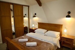Un letto ben rifatto con due cuscini e due asciugamani, una testiera in legno, comodini con lampade e un armadio in legno.