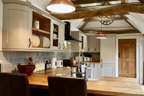 A kitchen with wooden beams, white cabinets, and a wooden dining table with chairs. - Cotswolds Grade II Listed Barn +underfloor heating (Little Rissington)