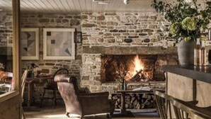 Una chimenea de piedra con fuego, un sillón de madera y una mesa con un jarrón de flores.