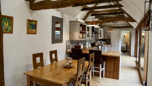 Un comedor con una mesa y sillas de madera, una cocina con armarios blancos y un dormitorio en lo alto con techo inclinado.