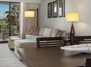 Ein Hotelzimmer mit einer Couch, einem Esstisch, einer Lampe und Blick ins Freie.