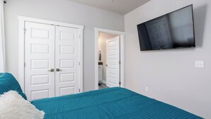 A bedroom with a teal bedspread, white doors, a TV on the wall, and a ceiling fan. - H4 Spacious & Urban Modern Condo - Great Location! (Oklahoma City)
