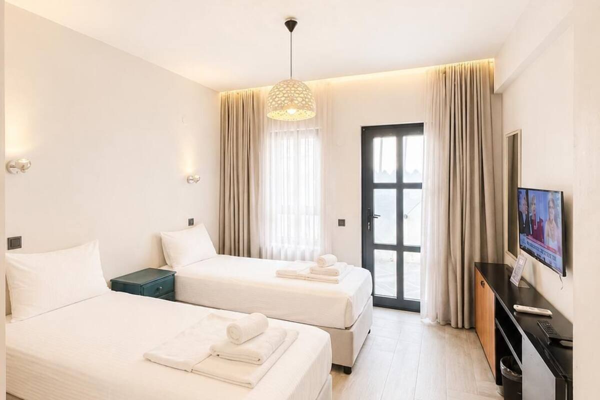 Habitación de hotel con dos camas, televisión, escritorio y ventana con cortinas.