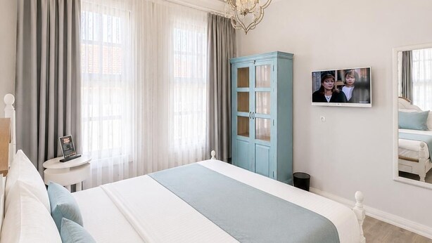A modern hotel room with a large bed, a TV, a wardrobe, and a chandelier. - Alada Saphire Bozcaada (Bozcaada)