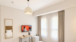 A hotel room with a bed, a TV, a desk, and a window with curtains. - Alada Saphire Bozcaada (Bozcaada)