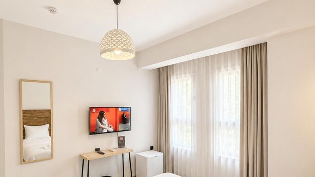 Una habitación de hotel con cama, televisor, escritorio y ventana con cortinas.