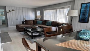 Ein modernes Wohnzimmer mit einem Ecksofa, einem Glastisch und einem Essbereich mit einem Tisch mit Glasplatte.