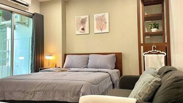 A bedroom with a bed, a bedside table, a lamp, a sofa, and a wall-mounted shelf with a plant.