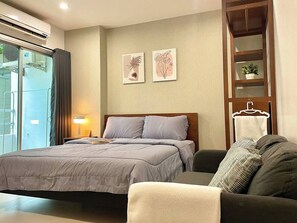 A bedroom with a bed, a bedside table, a lamp, a sofa, and a wall-mounted shelf with a plant. - Low rise 1min BTS | EmDistrict Mall | A/C | Wi-Fi (Watthana)