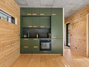 Eine moderne Küche mit grünen Schränken und Holzelementen, einem eingebauten Backofen und einem Fenster mit Blick ins Freie.